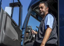 A man standing at the driver entrance of a blue work truck.