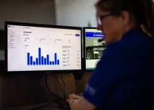 A monitor with a bar graph with a person sitting next to it wearing a headset.
