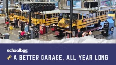 School bus maintenance garage with several yellow buses undergoing service, mechanics working in repair bays, and overhead equipment. Graphic reads “A Better Garage, All Year Long” with the School Bus Fleet logo.