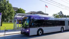 A purple and white CDTA bus parked at a bus stop.