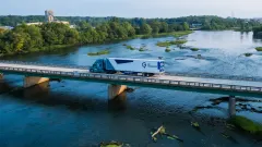 A GP Transco tractor-trailer crosses a bridge over a river, with trailer side skirts visible beneath the white trailer.