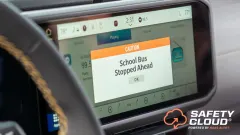 Vehicle dashboard display showing a “Caution: School Bus Stopped Ahead” warning from HAAS Alert’s Safety Cloud system, designed to alert motorists to stopped school buses.