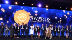 A group of 2026 APTA Award recipients pose onstage with medals and trophies in front of a large APTA Awards backdrop during the awards ceremony.