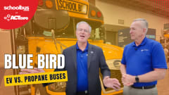 Two Blue Bird executives stand in front of a school bus at ACT Expo while discussing propane and electric school bus technology, infrastructure, and alternative fuel options.