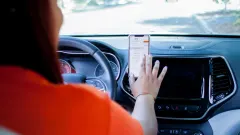 A driver in an orange t-shirt uses a smartphone mounted on a vehicle dashboard to access HopSkipDrive’s app.