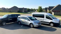 Three Sunrise-branded student transportation vehicles — a black SUV, silver minivan, and white passenger van — parked together in a residential neighborhood.
