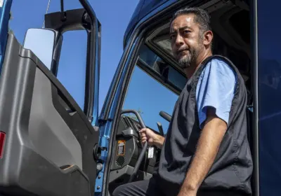 A man standing at the driver entrance of a blue work truck.