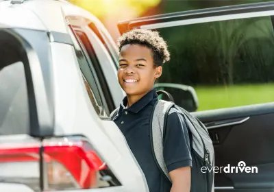 Student wearing a backpack stands beside an open passenger vehicle in an EverDriven alternative student transportation image.