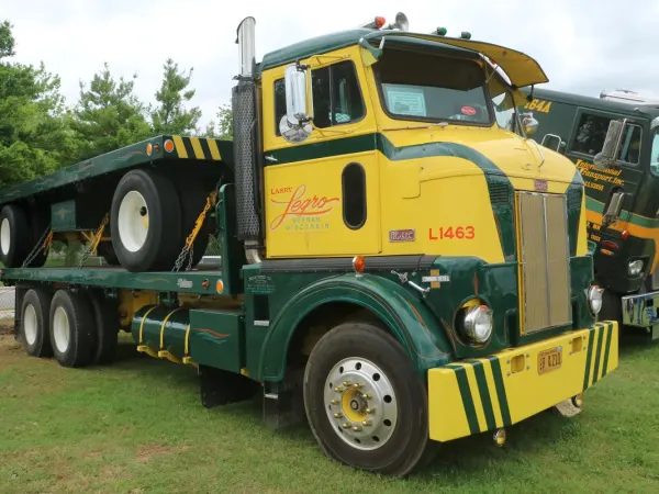 A yellow and green "bubblenose" cabover truck from the 1940s with vintage flatbed trailer