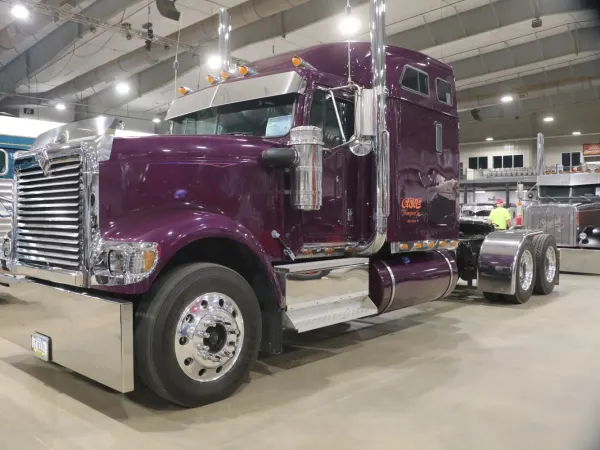 Plum-purple conventional International 9900 truck with sleeper on display indoors