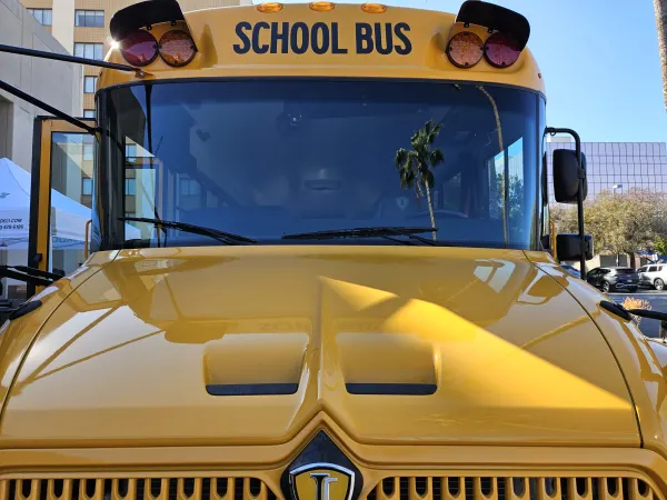a close up of the front of a school bus with a palm tree reflection in the windshield