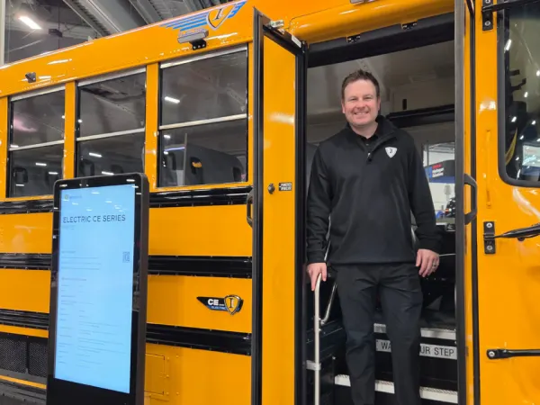 Alec Borror stands in the doorway of an IC Bus electric CE Series school bus displayed on the ACT Expo show floor.