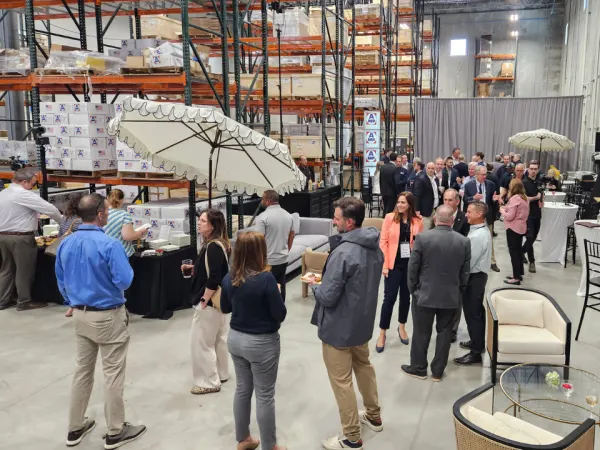 A group of people standing in the new AMF Bruns warehouse during a grand opening with refreshments.