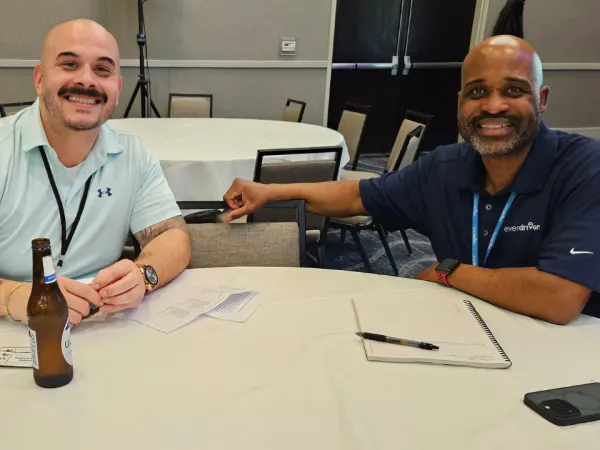Two attendees smile while seated at a networking table during a meet-and-greet event sponsored by EverDriven.
