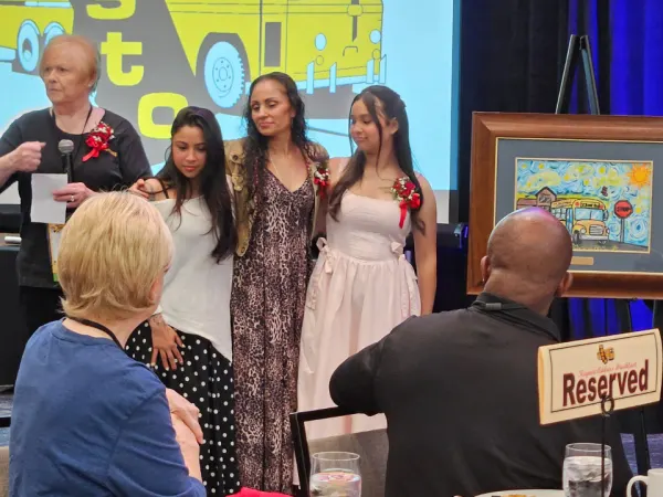 Students and presenters stand beside a framed school bus safety poster during an awards presentation recognizing contest winners.