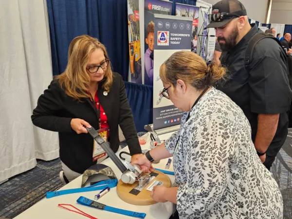 Attendees visit the AMF Bruns vendor booth in the expo hall, examining a wheelchair securement device while speaking with an exhibitor about safety equipment.