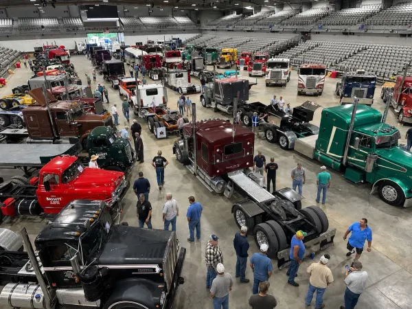 People walking among antique trucks inside a show arena