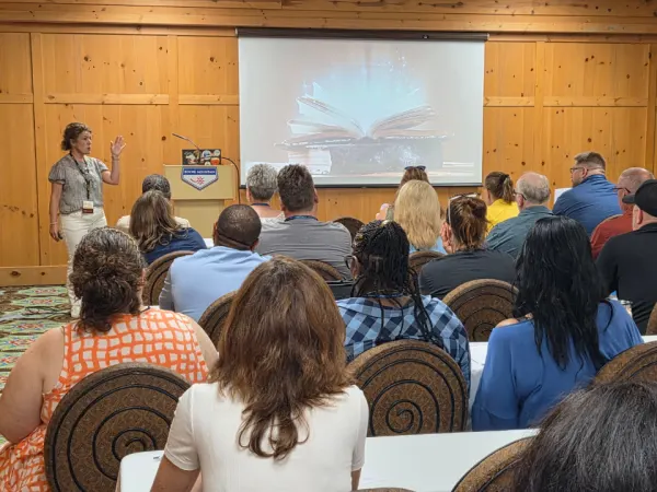 Jen Laidlaw presents to a packed room of conference attendees during an educational session, speaking from the front of the room while participants watch a presentation screen.
