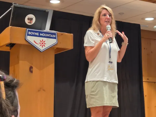 Executive Director Katrina Morris speaks on stage at the Michigan Association for Pupil Transportation conference, holding a microphone while addressing attendees.