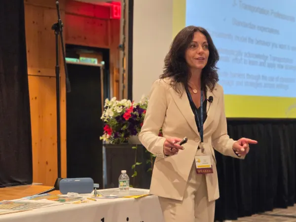 Child Behavior Consulting founder Lisa Navarra presents an educational session, speaking to attendees while standing beside a presentation screen and training materials.