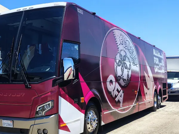 A maroon Qatar team motorcoach operated by Lux Bus America stands ready for service. 
