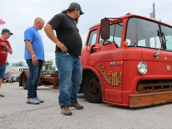 People looking at a very low-riding modified vintage Ford cabover truck