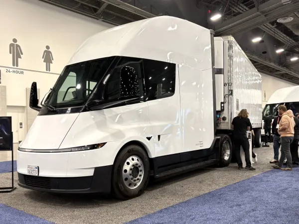 White streamlined Tesla electric Class 8 tractor on show floor with people standing near front of trailer