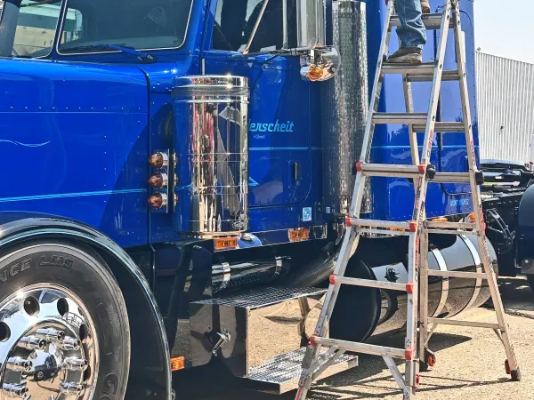 Man standing on ladder polishing exhaust stacks on a blue classic truck.