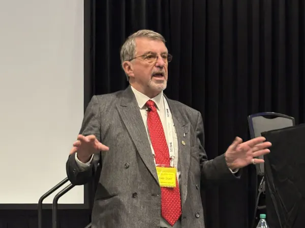 Man in sport jacket and red tie speaking to audience