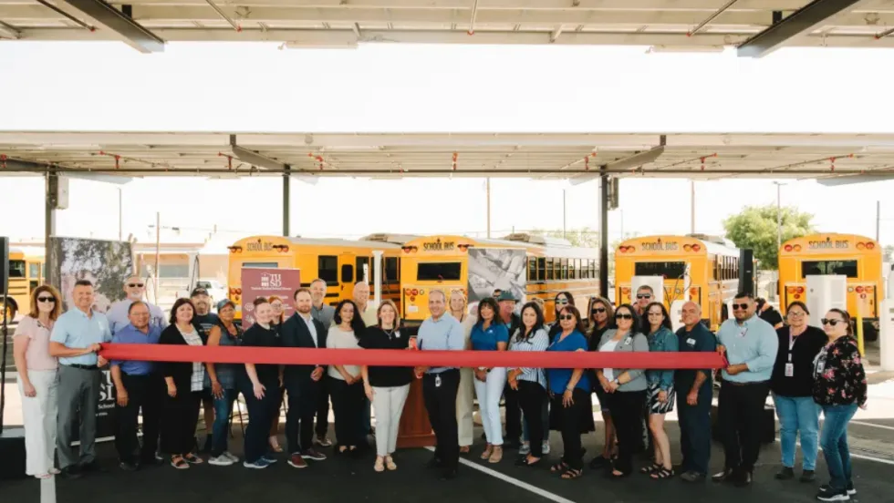Turlock Unified staff and partners hold a ribbon-cutting in front of new electric school buses under solar canopies at the district transportation center.