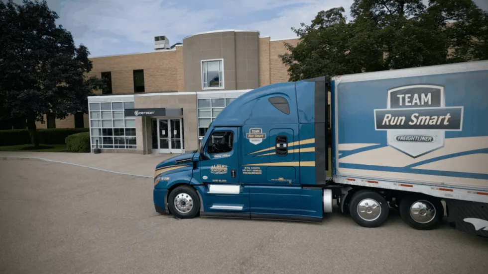 A blue Freightliner Cascadia truck operated by Albert Transport and branded with the Team Run Smart logo parked outside a Detroit Diesel facility.