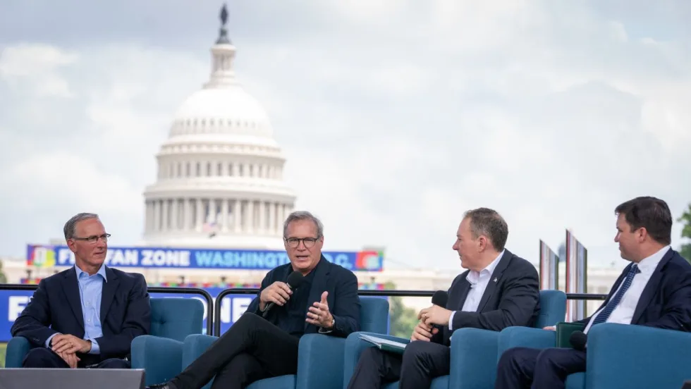 Four men in suits on the National Mall with giant video screen showing capitol building in the background