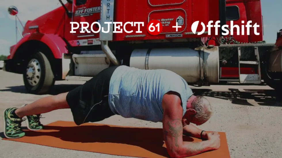 Truck driver doing a plank exercise on a mat with a red truck in the background.
