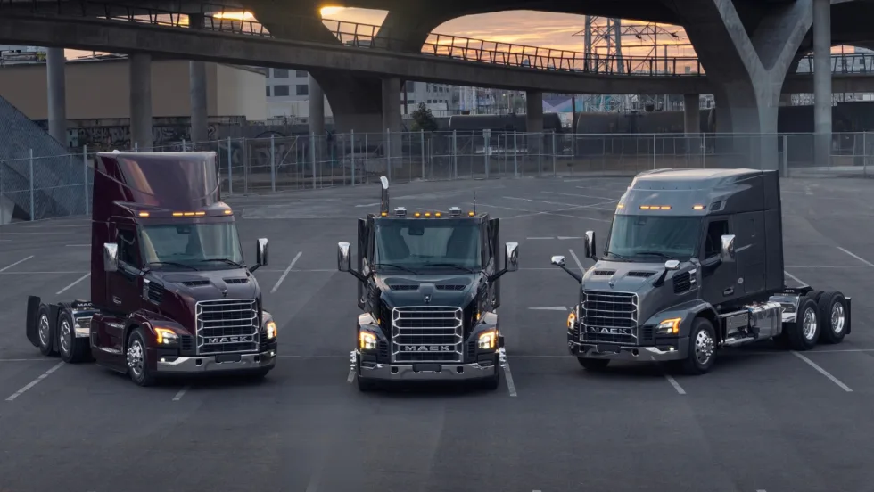 Three Mack Anthem heavy-duty trucks parked side by side beneath an overpass, including two highway tractors and a vocational truck.