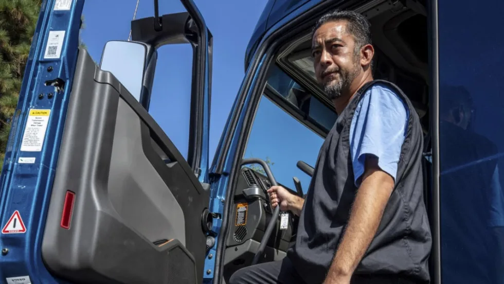 A man standing at the driver entrance of a blue work truck.
