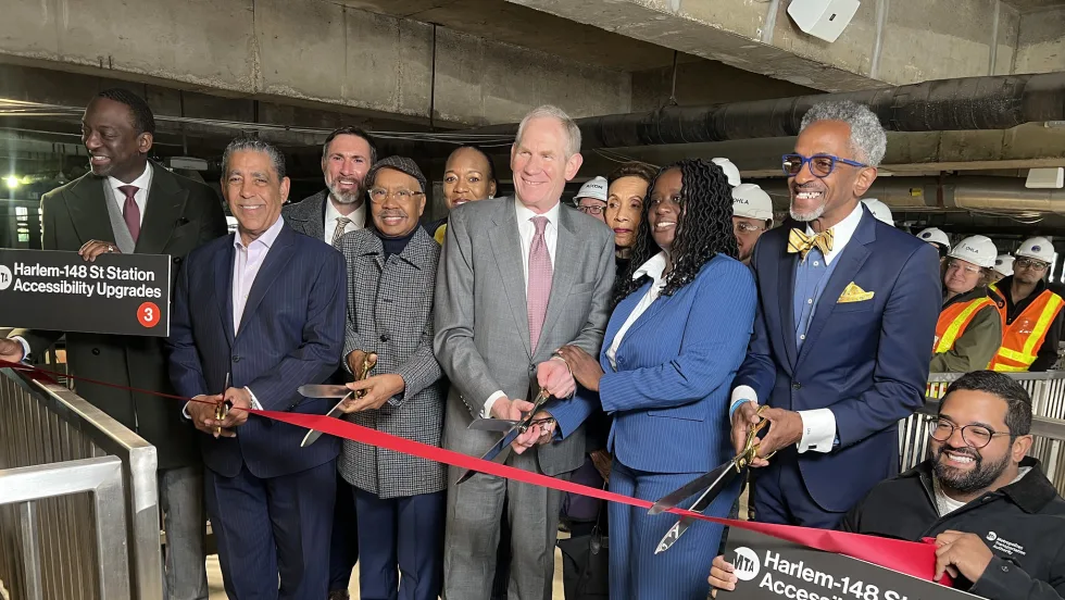 A group of people stand in the Harlem-148 Street 3 Station and pose during a ribbon cutting ceremony.