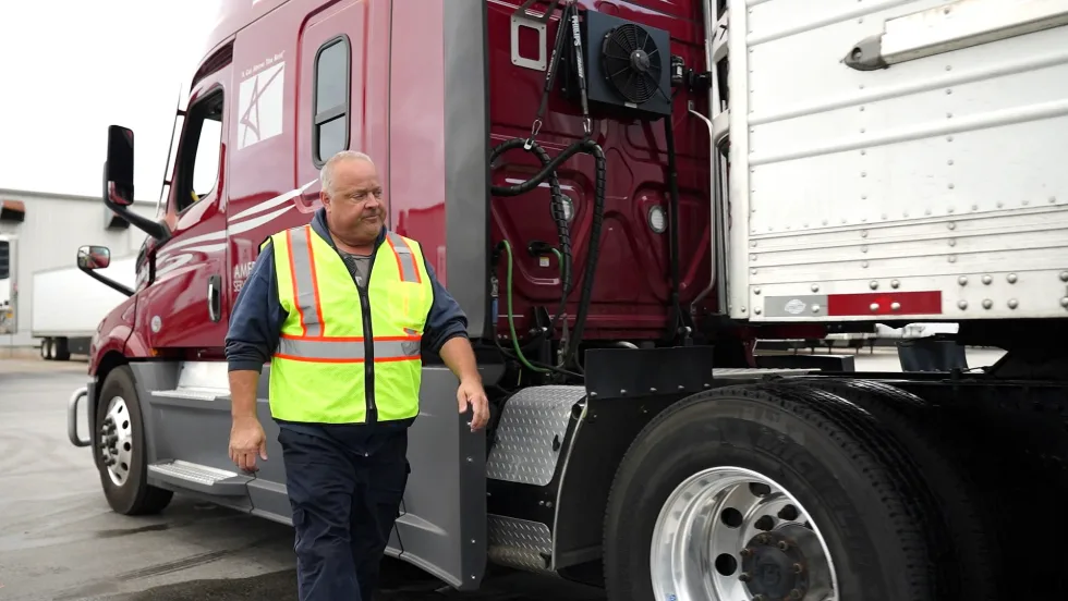 Photo of truck driver in yellow safety vest walking alongside tractor-trailer