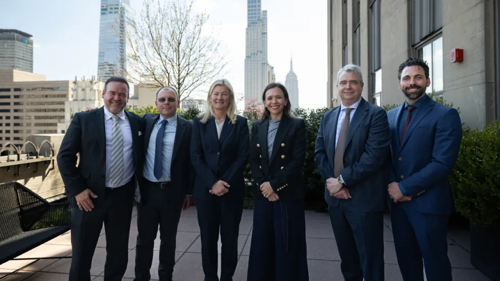 Six people in business wear pose for a picture in front of the Empire State Building in the distance.