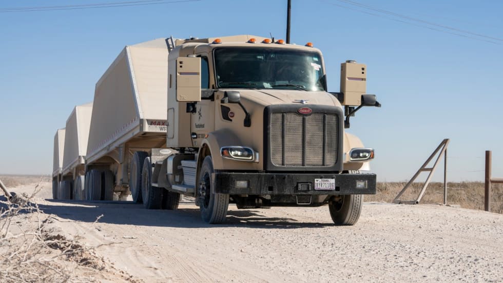 Khaki-colored autonomous Peterbilt truck hauling triple trailers loaded with frac sand for Atlas Energy Solutions in the Permian Basin.