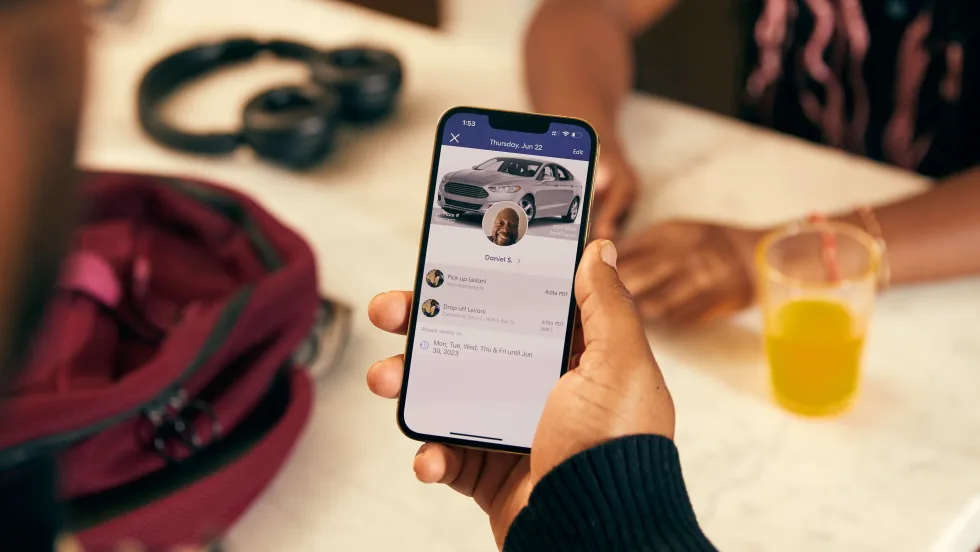 A close up image of a hand holding a phone with HopSkipDrive's platform and CareDriver information on the screen.