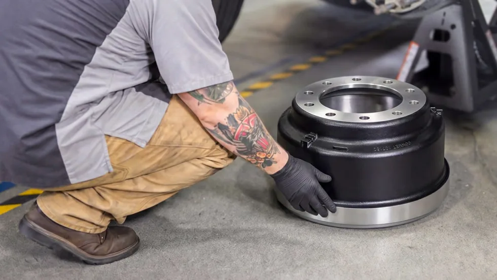 Heavy duty truck technician crouched down replacing brake drum