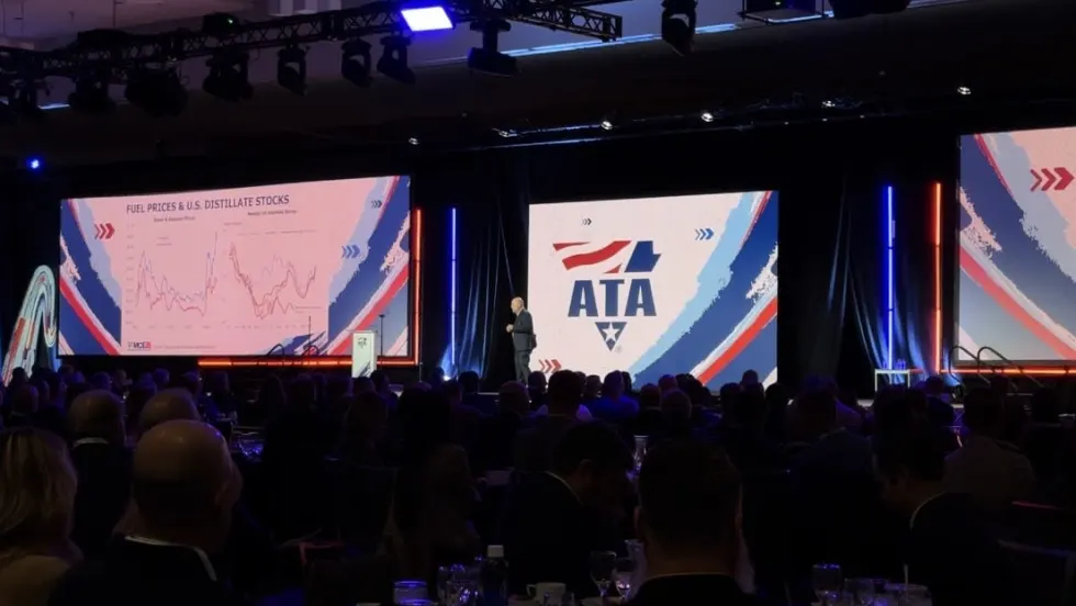 Man on large stage with American Trucking Associations logo in the background and large screen displays of distillate stocks.