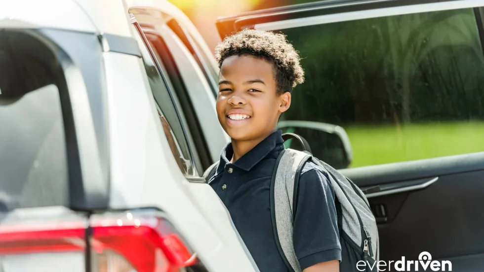 Student wearing a backpack stands beside an open passenger vehicle in an EverDriven alternative student transportation image.