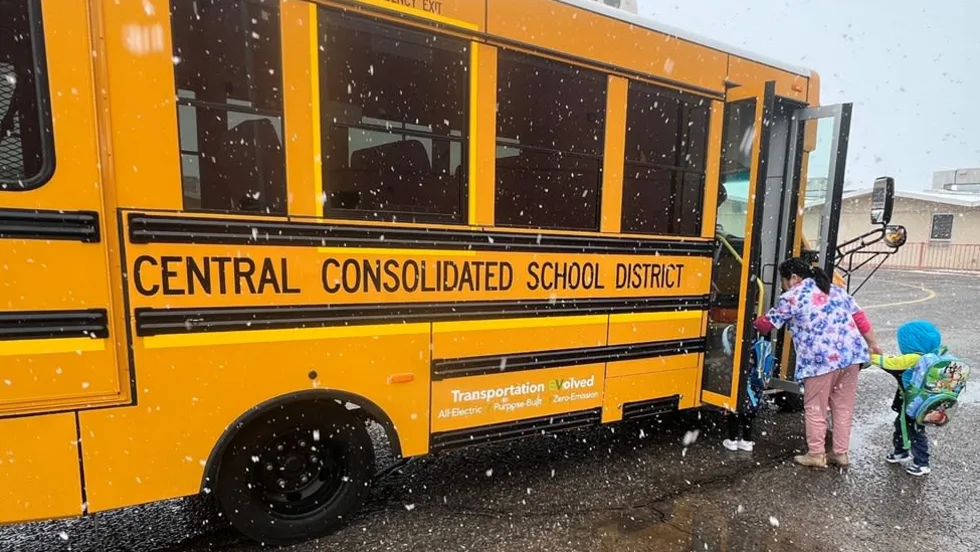 Children board a yellow electric school bus from Central Consolidated School District during snowfall, as an adult assists students at the bus entrance.