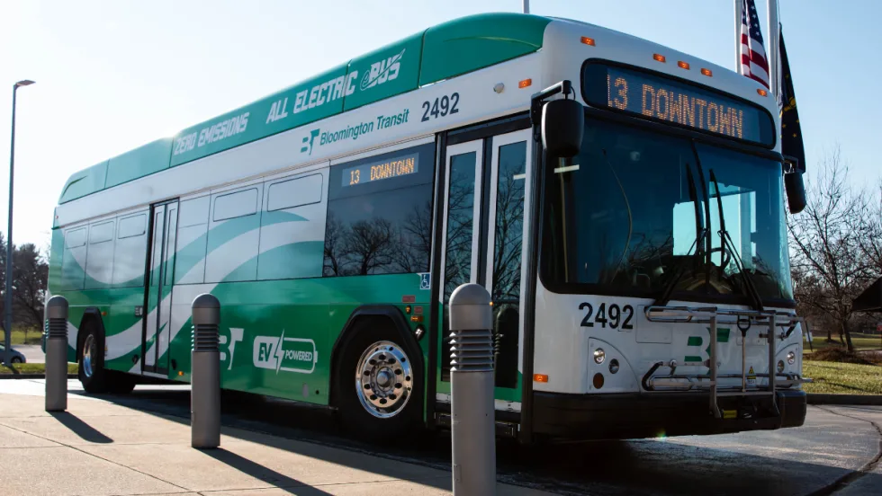 A green and white Bloomington Transit electric bus parked in the street.