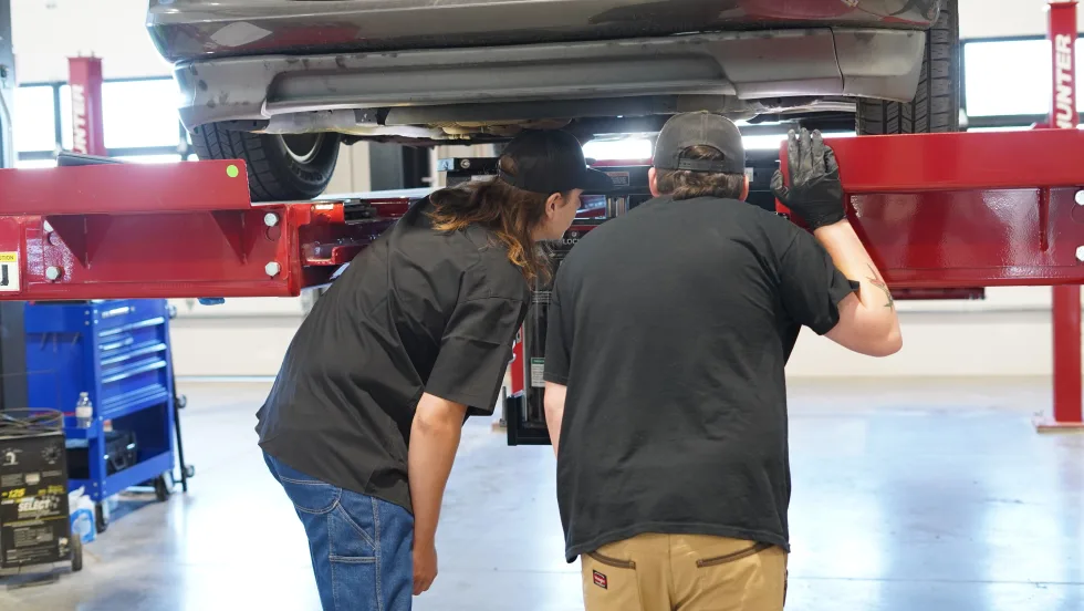 Maintenance officials examining a vehicle on a lift.