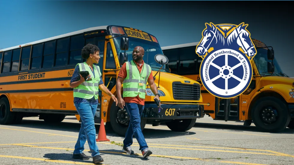 Two First Student drivers walking in front of school buses with a Teamsters logo in the foreground.