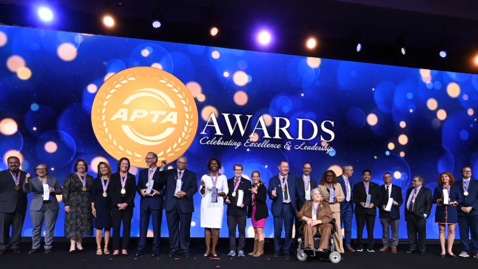 A group of 2026 APTA Award recipients pose onstage with medals and trophies in front of a large APTA Awards backdrop during the awards ceremony.