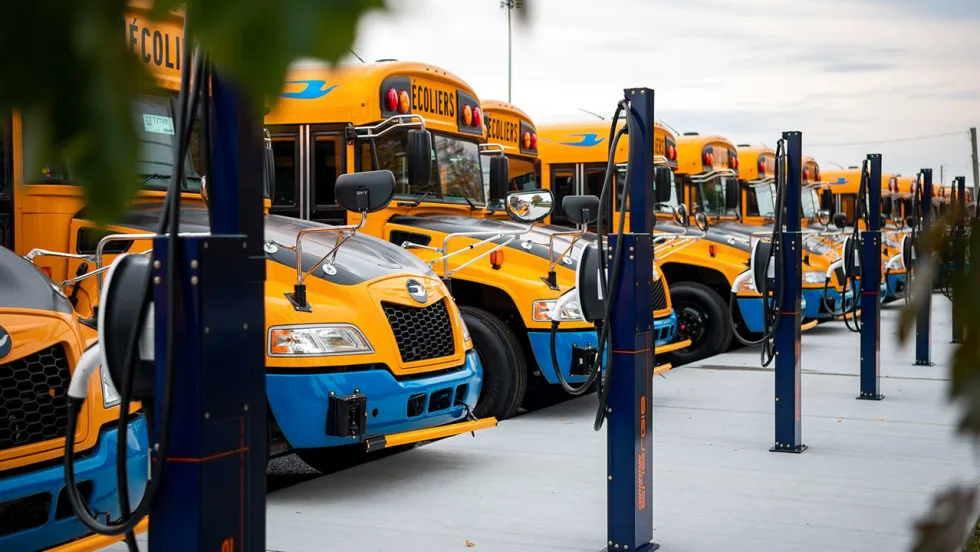 Electric school buses connected to charging stations at a fleet depot supporting zero-emission transportation infrastructure.