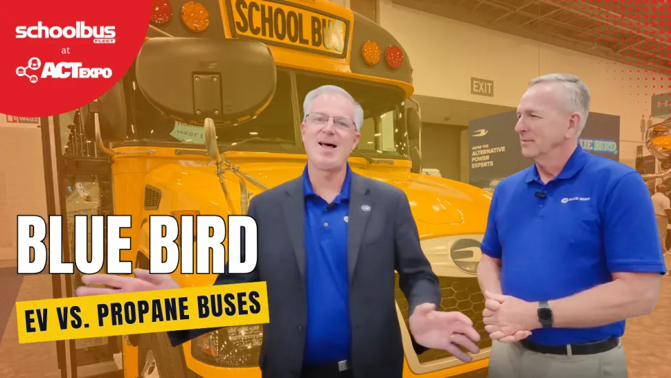 Two Blue Bird executives stand in front of a school bus at ACT Expo while discussing propane and electric school bus technology, infrastructure, and alternative fuel options.